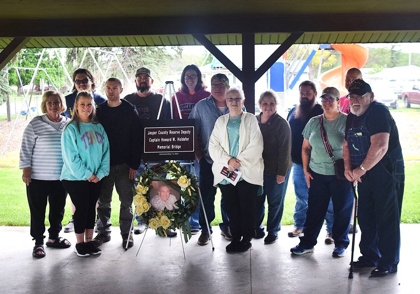 Family members of Howard Holdefer pose for a photo next to a wreath bearing his image and the replica of a sign that appears near a bridge named after the reserve deputy who died more than 50 years ago. The bridge over the South Skunk River on F-62, just west of Reasnor, has been renamed to Jasper County Reserve Deputy Captain Howard W. Holdefer Memorial Bridge.