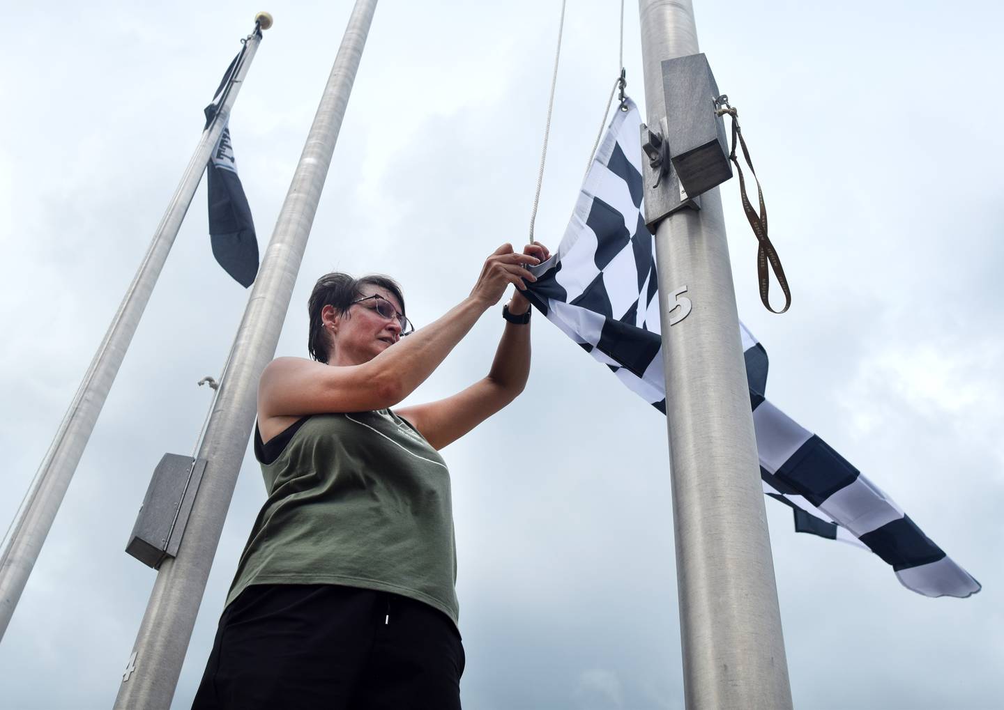Erin Yeager, executive director of Newton Main Street, prepares to hoist a finish line flag to a post on June 25 in downtown Newton. She was joined by IndyCar representatives who helped place flags around the town square to commemorate the upcoming race weekend at Iowa Speedway.
