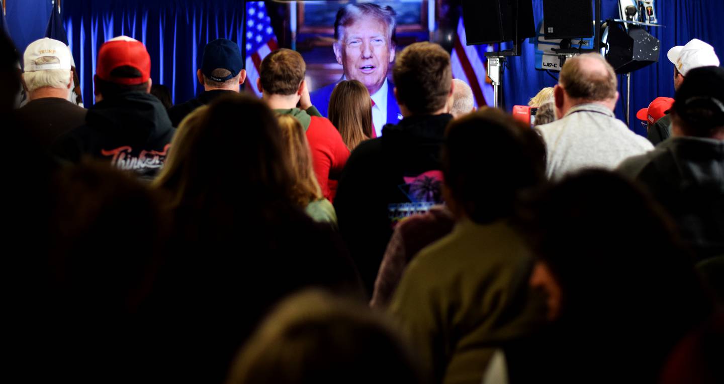 Supporters of Donald Trump watch a video of the former president speaking to them about the Iowa caucuses and supporting his campaign.